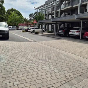 Neu gepflasterte Straße mit mehreren geparkten Autos neben einem mehrstöckigen Gebäude unter bewölktem Himmel