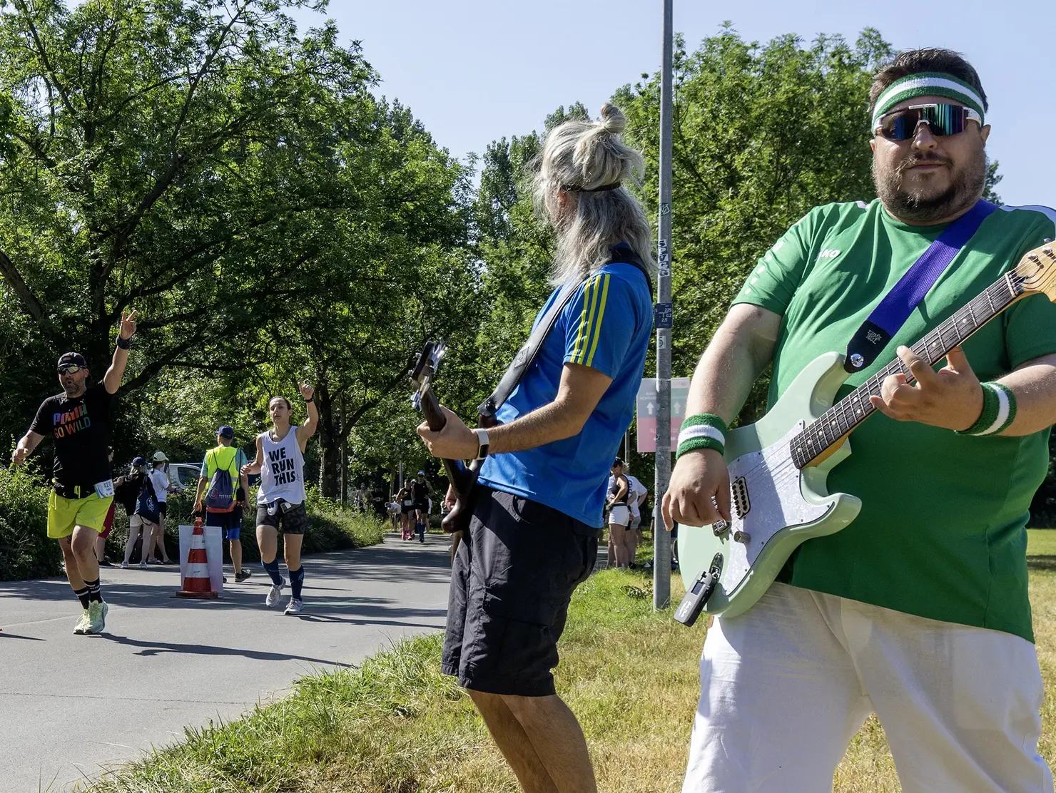 Zwei Gitarristen einer Rockband und Läufer, die vorbeilaufen. Klick öffnet Bild in größerer Ansicht.