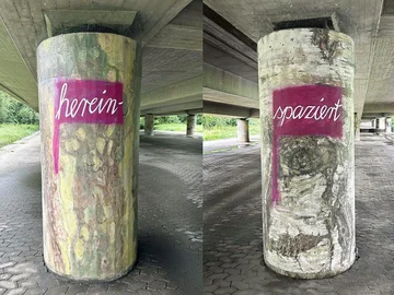 Zwei Brückenpfeiler der Ludwigsbrücke, bemalt von Sabine Deifel als Baumstämme mit den weißen Schriftzügen 'herein-' und 'spaziert' auf rotem Hintergrund.