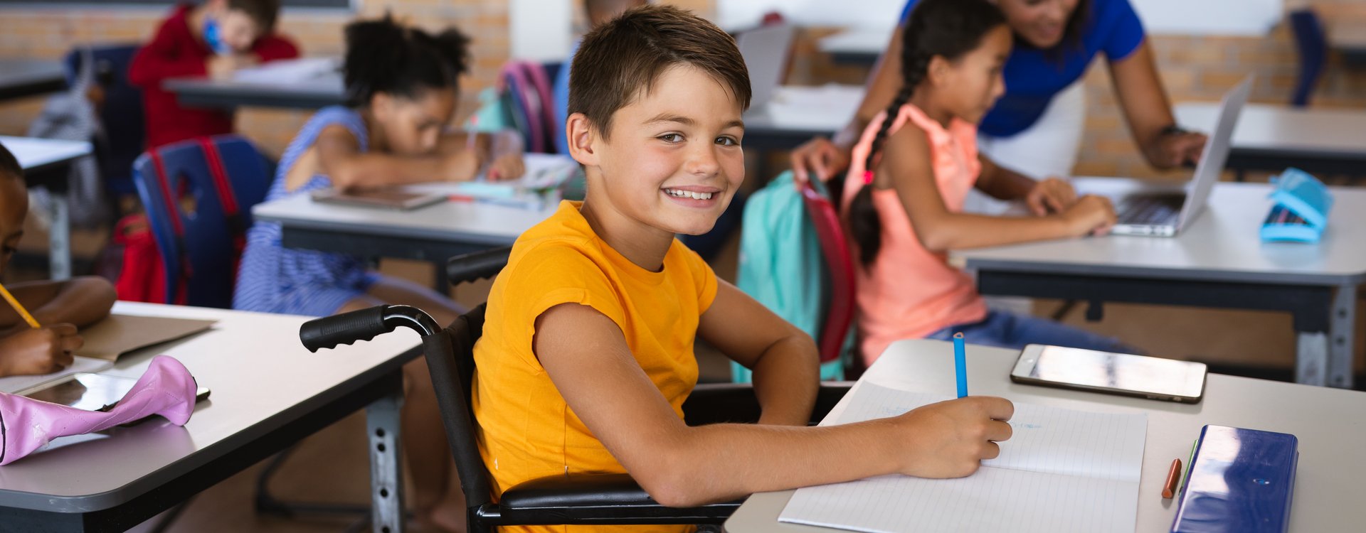 Portrait eines lachenden Jungen im Rollstuhl während einer Unterrichtsstunde in der Grundschule.