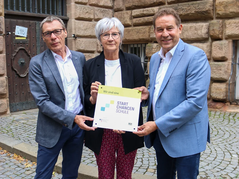 Gruppenbild mit Brehm, Schirner und Braun, die ein Schild halten mit dem Text "Wir sind eine Start-Chancen-Schule".