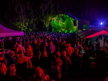 Menschenmenge bei einem Konzert mit buntem Konfetti und Bühnenbeleuchtung im Hintergrund