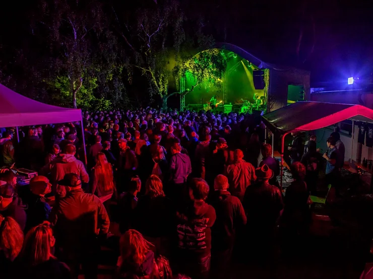Menschenmenge bei einem Konzert mit buntem Konfetti und Bühnenbeleuchtung im Hintergrund