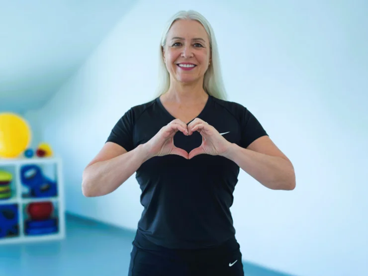 Patricia Hein formt mit den Händen ein Herz vor dem Oberkörper.