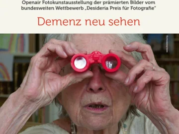 Ältere Person hält rote Spielzeugferngläser vor die Augen