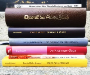 Sechs übereinander liegende Bücher mit Titeln und Autoren auf den Buchrücken, darunter "Chronik der Stadt Fürth" und mehrere Werke von Jakob Wassermann