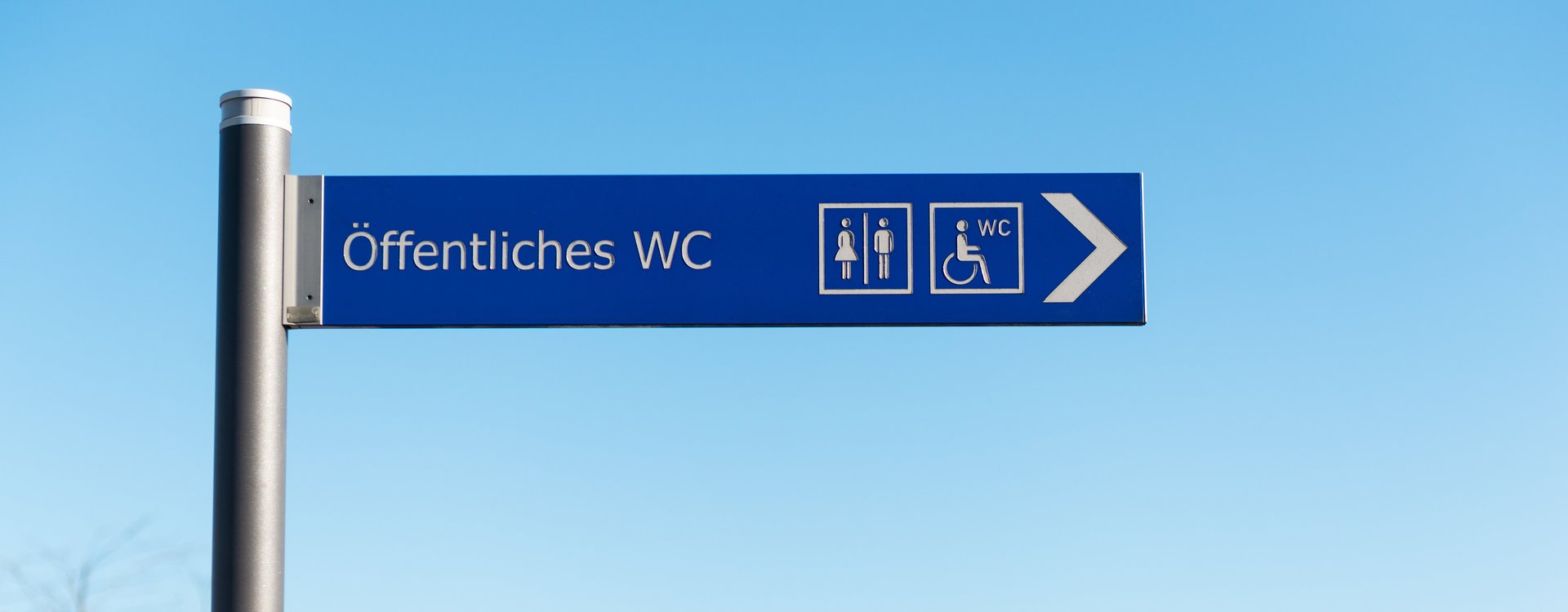 Barrierefreie Toiletten Wegweiser mit der Aufschrift "Öffentliche Toilette" und den Zeichen für Mann, Frau und barrierefreie Toilette
