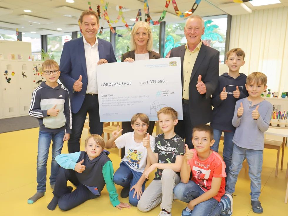 Bürgermeister Markus Braun, bayerische Familienministerin Ulrike Scharf, und Oberbürgermeister Thomas Jung mit den Jungs in einem städtischen Kinderhort mit einem Förderscheck in der Hand.