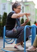 Eine Frau kommuniziert in Gebärdensprache mit einem Mädchen während sie auf einem Spielplatzkarussell sitzen.