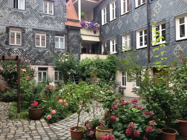 Blick in einen aufwändig begrünten Innenhof, umrahmt von schwarzen Schieferfassaden.
