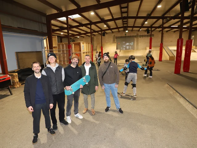 Gruppenfoto der beteiligten Personen in der Halle und skatende Jugendliche im Hintergrund. Klick öffnet die Meldung.