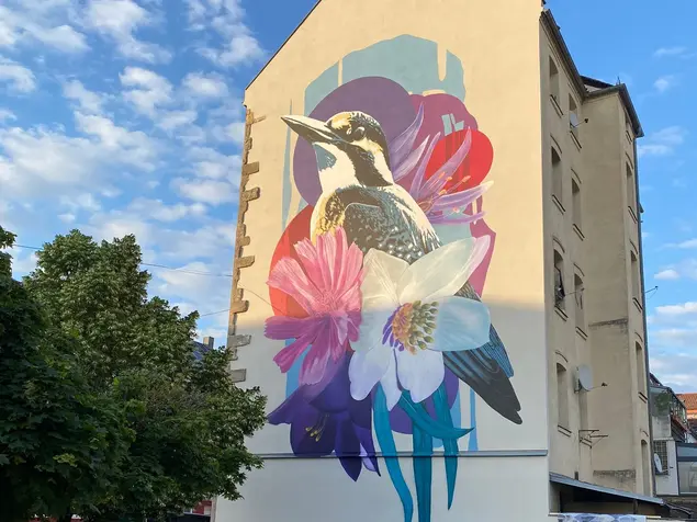 Großflächige Malerei an der Fassade eines vierstöckigen Hauses: Florale Motive und ein großer Eisvogel.