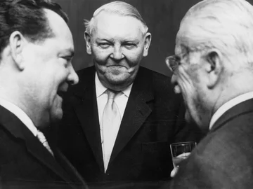 Schwarz-weiß-Aufnahme von Max Grundig, Ludwig Erhard und Gustav Schickedanz, die in einer Gesprächssituation stehen.