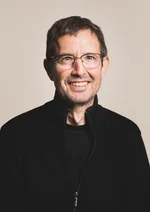 Mann mit dunklem Oberteil vor einfarbigem Hintergrund