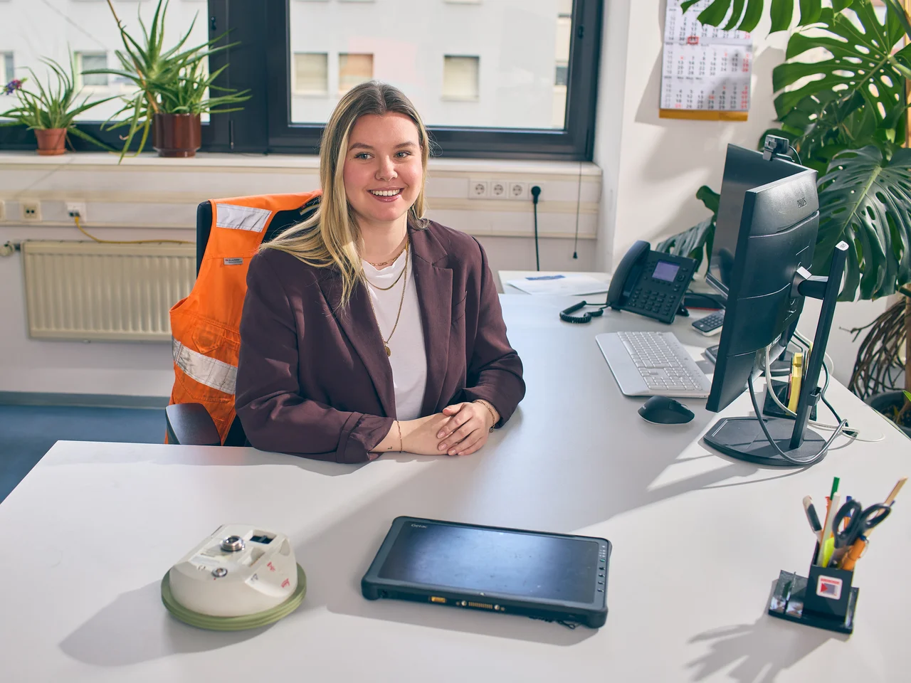Junge Frau sitzt an einem Schreibtisch mit Warnweste auf dem Bürostuhl. 