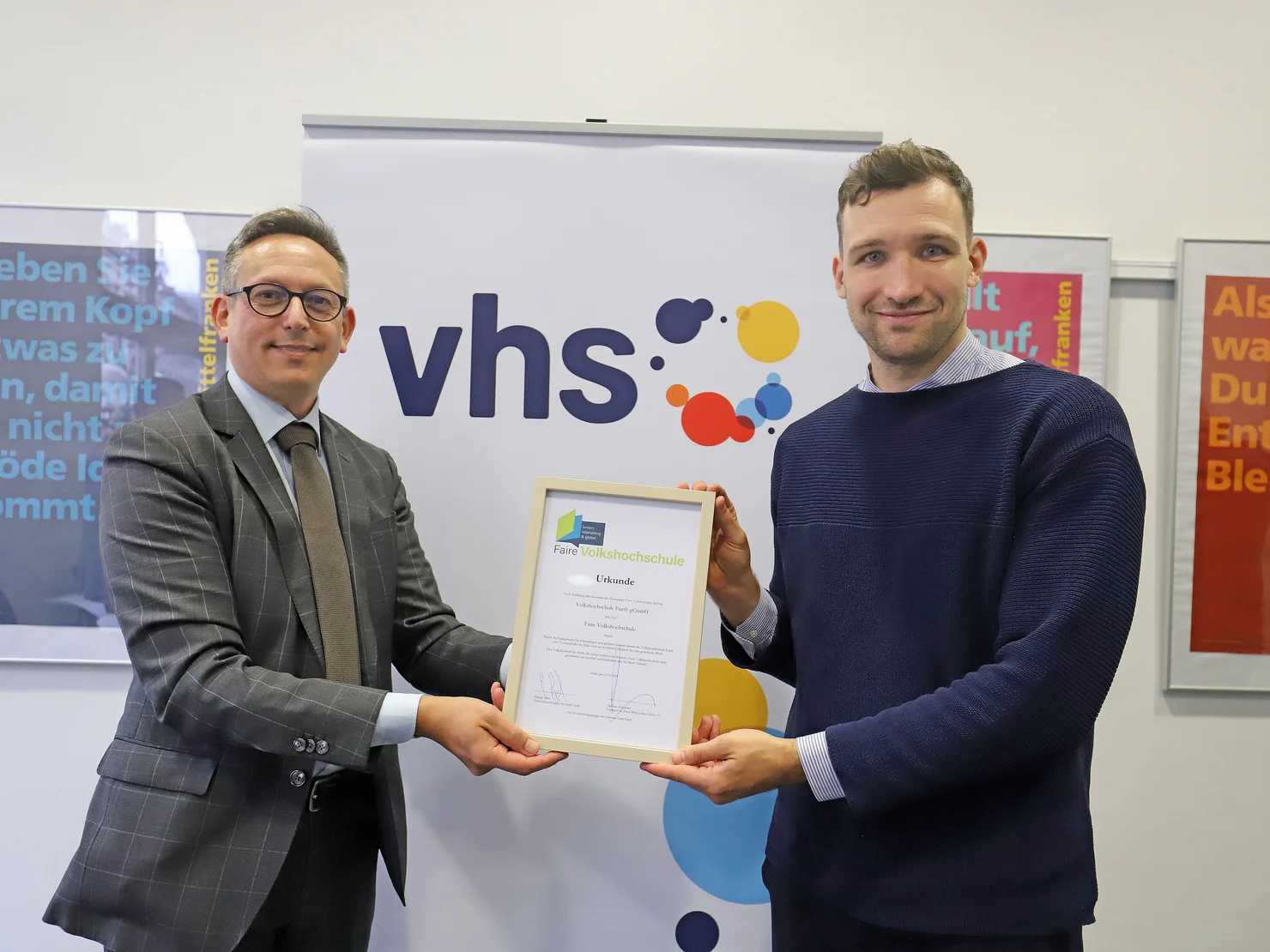 vhs-Chef Felice Balletta, und Fairtradebeauftragter Philipp Abel präsentieren zusammen die Urkunde. Klick öffnet Bild in größerer Ansicht.