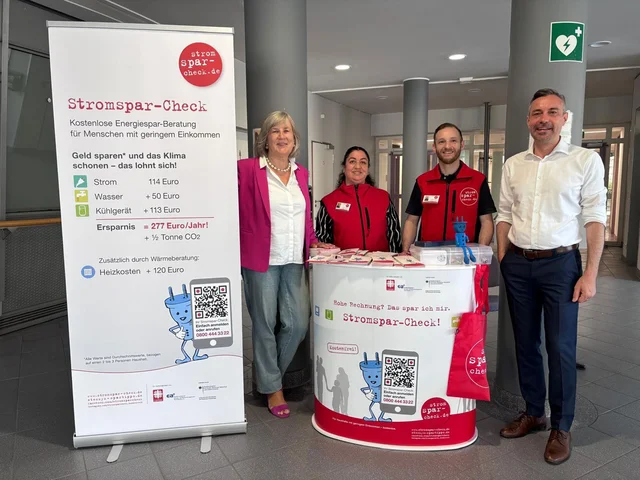 Döhla, Demir, Wunder und Bayer-Tersch stehen neben einem Informationsstand mit einem Banner und einem Tisch, die für den Stromspar-Check werben. Klick öffnet die Meldung.