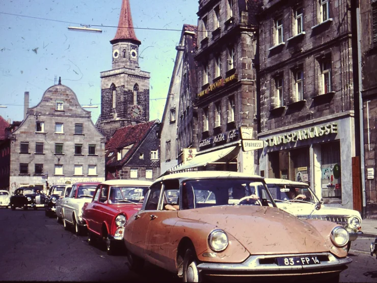 Historische Straßenszene aus den 70er Jahren mit mehreren geparkten Autos und historischen Gebäuden im Hintergrund