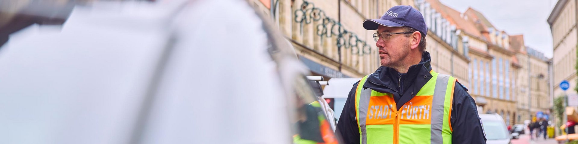 Ein Mitarbeiter der Straßenverkehrsordnung steht auf einer Straße neben einem geparkten Auto.