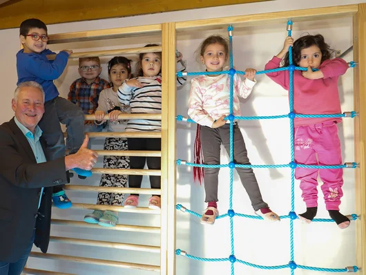 Jung mit Daumen-hoch-Zeichen und kletternde Kinder an einer Kletterwand. Klick öffnet die Meldung.