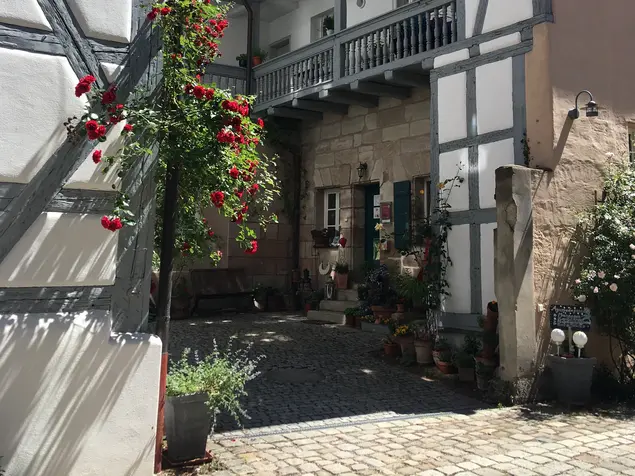 Blick zwischen zwei Fachwerkhäusern in den rosengeschmückten Innenhof.
