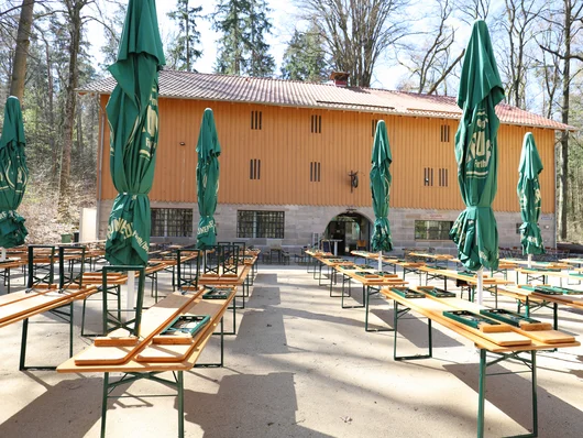 Die Waldgaststätte an einem sonnigen Tag mit Tischen und Bierbänken. Klick öffnet die Meldung.