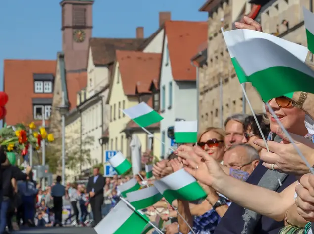 Zuschauende mit Fahnen in der Hand jubeln am Rande des Erntedankfestzugs.