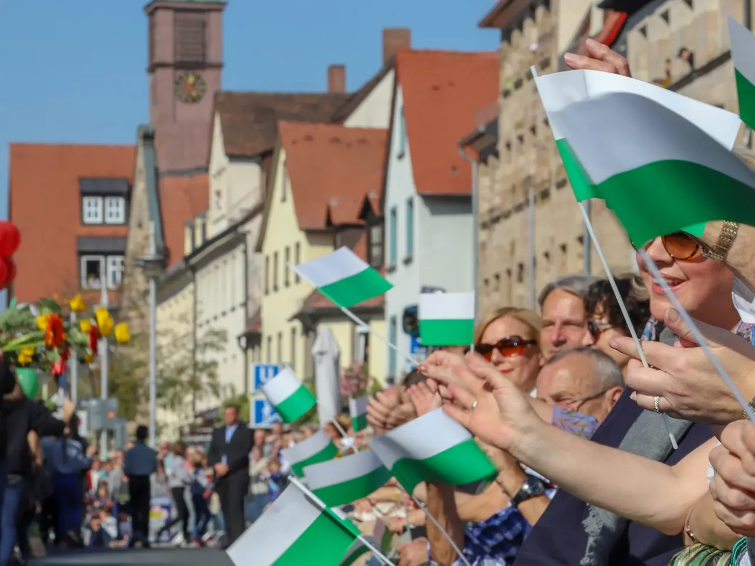 Zuschauende mit Fahnen in der Hand jubeln am Rande des Erntedankfestzugs.